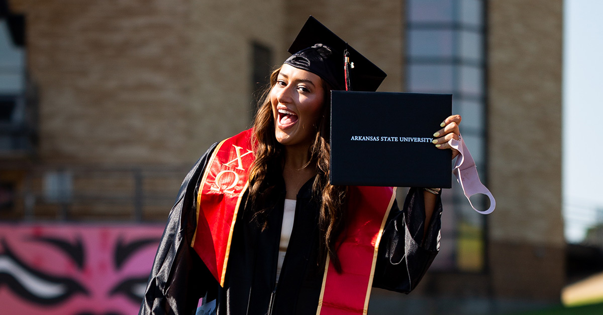 A graduate poses with her diploma cover at our 2020 Spring Commencement