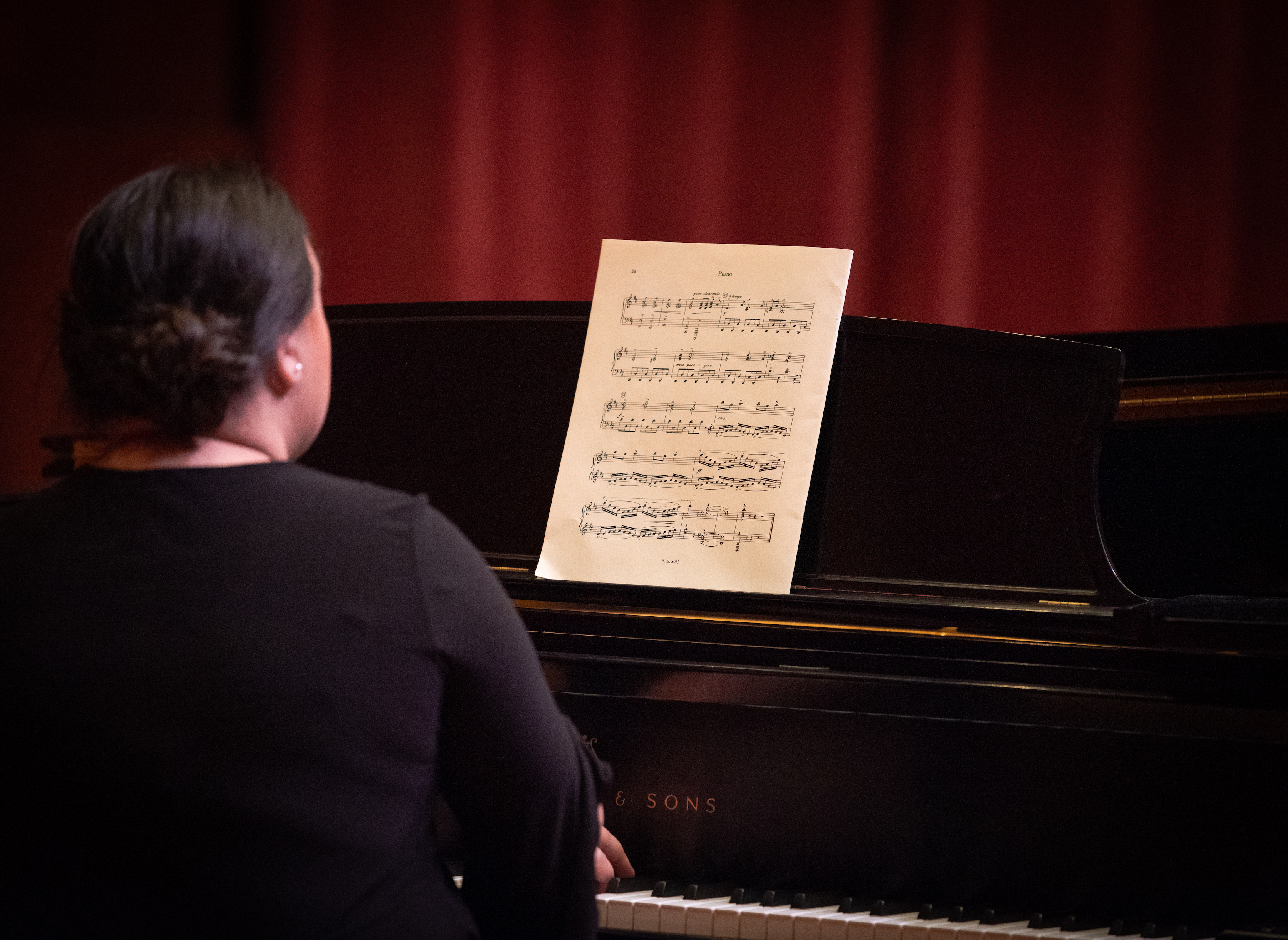 Backside of a pianist playing piano.  Single sheet of music on the piano.